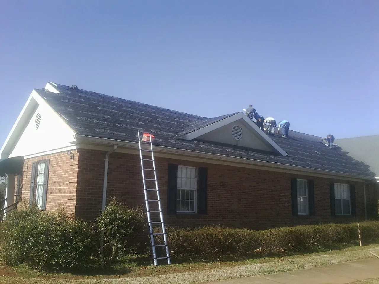 Crew tearing shingles off a brick ranch roof with a ladder set — Metal Roof Repair work by our crew in Veyo
