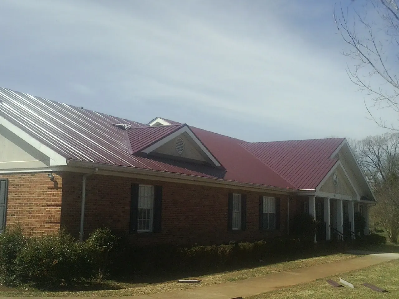 Red metal roof with gabled entries on a long brick building, from a Hail Damage Roof Repair job in Veyo