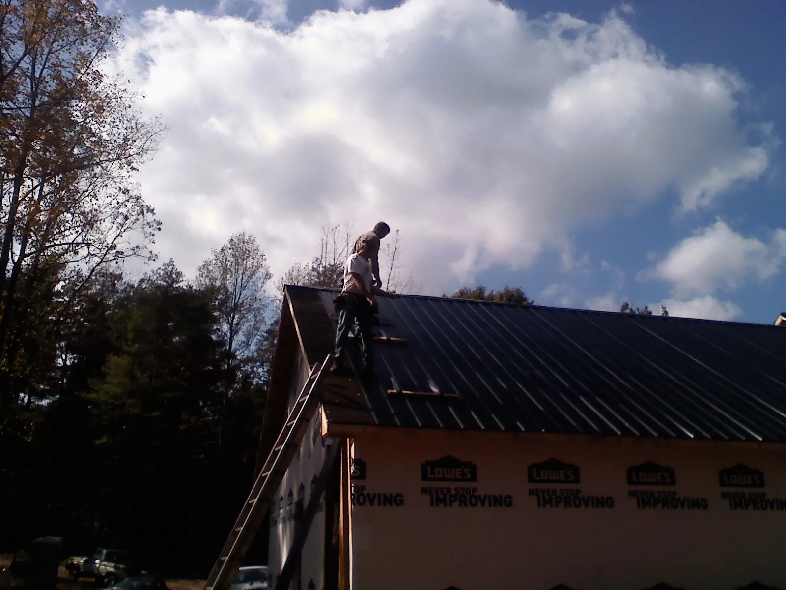 Roofer fastening dark metal panels high against a cloudy sky, from a Roof Inspection job in Veyo